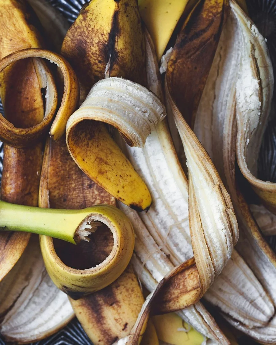 A heap of banana peels, some still yellow and some gone brown, curled open on a dark dish.